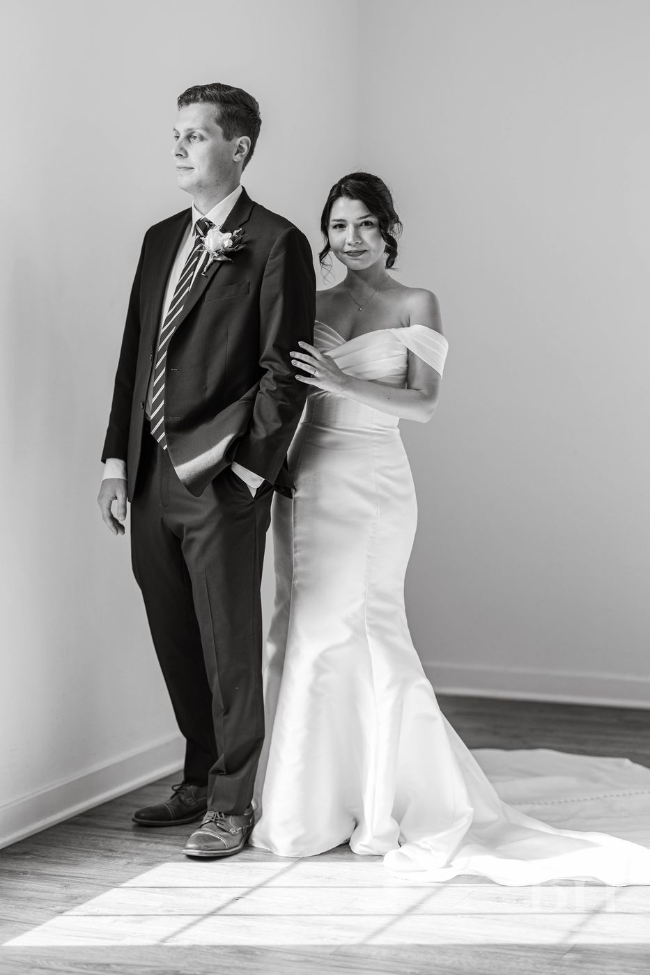 Groom and bride standing by a sunlit window, black and white